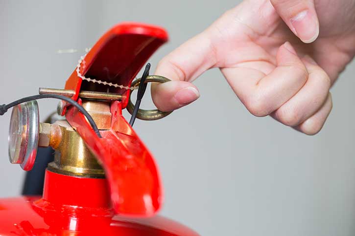 Pulling safety pin on fire extinguisher